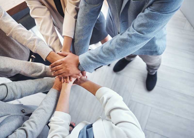 Group of people standing in a circle with their hands in the middle.