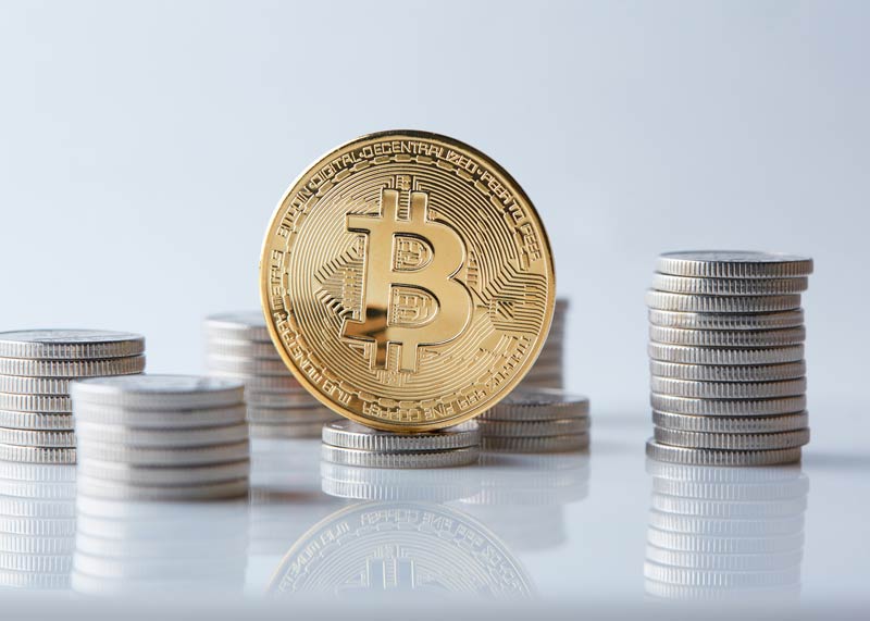 Stacks of silver coins with a large gold coin standing on end with the bitcoin icon on it.